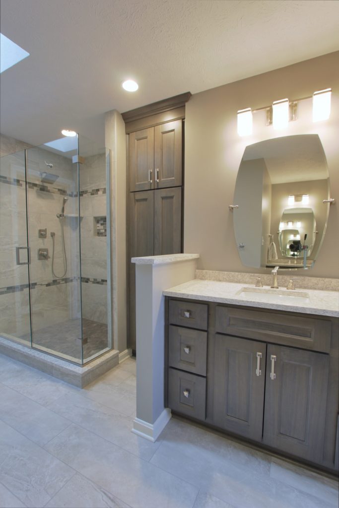 Modern bathroom design featuring transitional poplar shadow cabinetry, glass mosaic accents, and a spacious walk-in shower with a glass enclosure, complemented by elegant lighting and a sleek vanity with granite countertop.