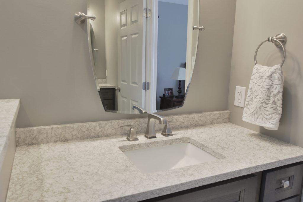 Modern bathroom vanity with polished countertop, sleek faucet, round mirror, and decorative towel on rack, showcasing transitional design elements in a remodeled space by Kingswood Designs.