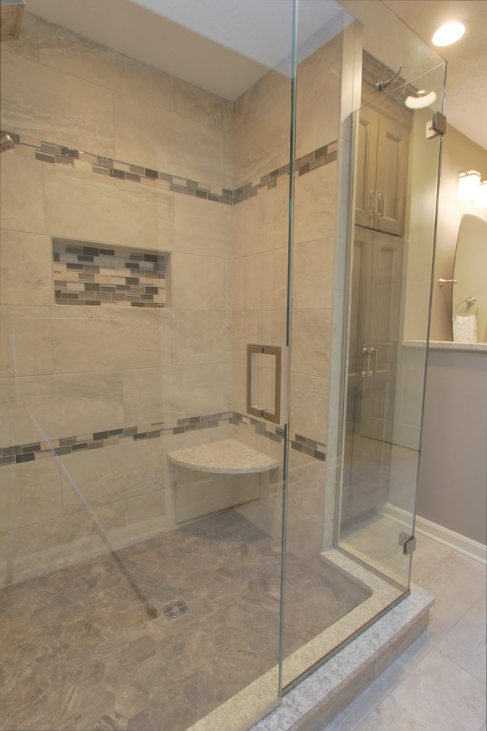 Transitional bathroom design featuring poplar shadow aspect cabinetry, glass mosaic accent stripes, and a shower surround with 12” x 24” horizontal staggered wall tiles and a 4” hexagon mosaic shower floor tile.