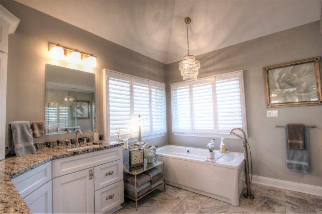 Traditional bathroom remodel featuring a freestanding tub, granite countertop with dual sinks, elegant chandelier, and natural light from window shutters in Bethel Park.