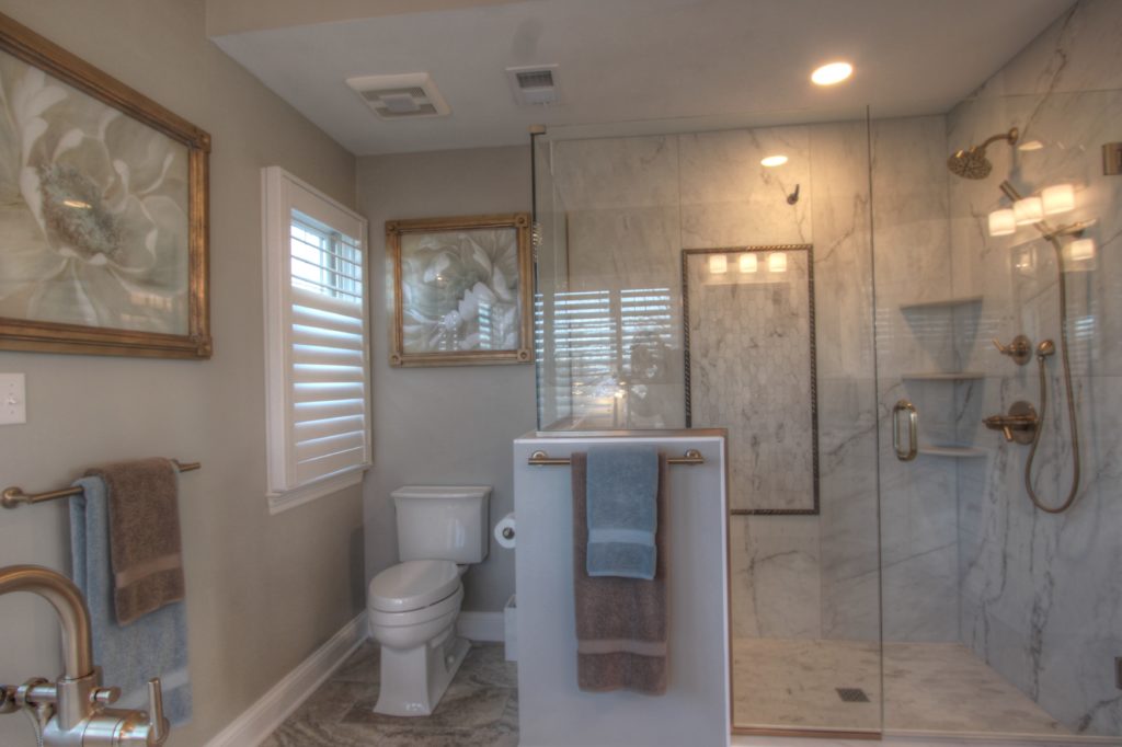 Traditional bathroom remodel in Bethel Park featuring a glass shower enclosure, marble walls, brushed bronze fixtures, and decorative floral artwork.