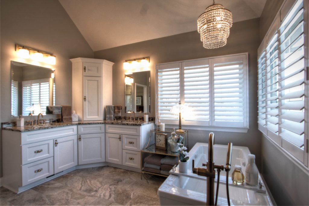 Traditional bathroom remodel featuring white cabinetry, granite countertops, elegant chandelier, and dual sinks with brushed bronze fixtures, showcasing a luxurious and functional design.