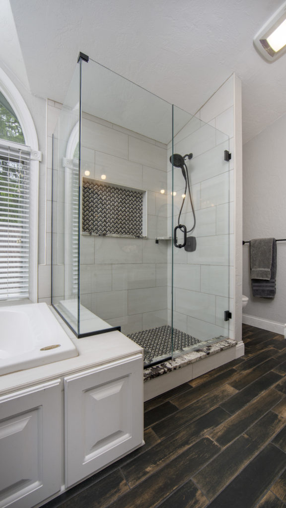 Modern farmhouse bathroom featuring a glass shower enclosure, custom tile work, and a freestanding tub, complemented by rustic tile flooring and matte black fixtures.