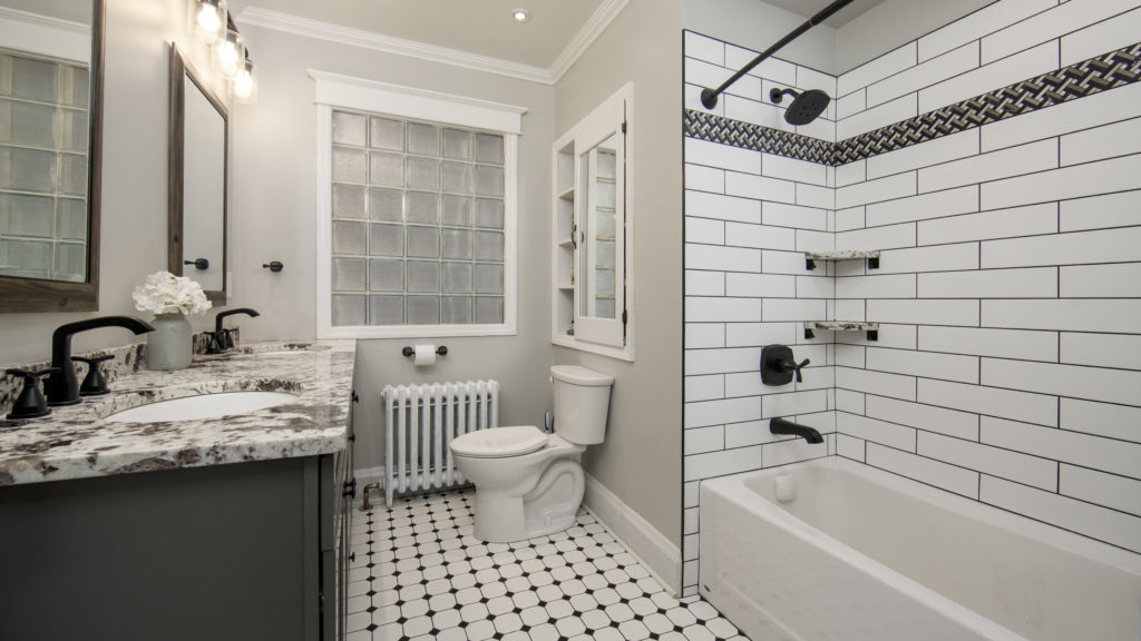 Modern farmhouse bathroom featuring Marsh Cabinetry with a painted grey finish, white subway tile shower with black grout, matte black fixtures, and a vintage-style black and white mosaic tile floor.